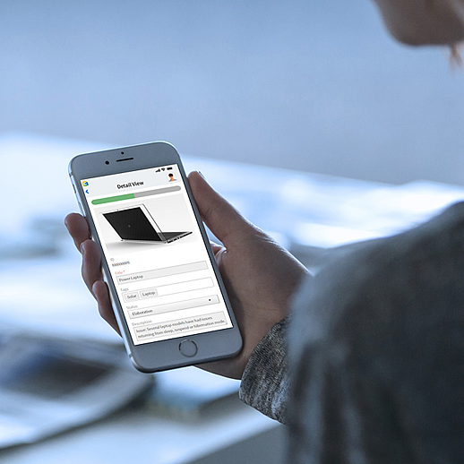 Frau hält ein Smartphone in der Hand mit der mobilen Detailansicht eines Produkts inklusive Produktbild eines Laptops, Statusleiste und Metadaten-Feldern