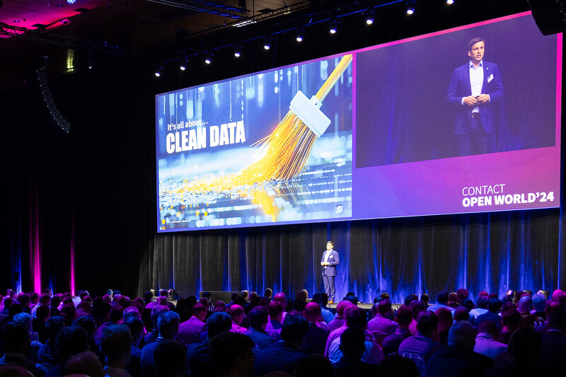 A conference stage with a man on it, an audience in front of it, and a slide that says “It's all about CLEAN DATA”.