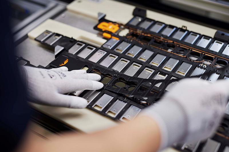 A person wearing white gloves assembles cell contact systems.
