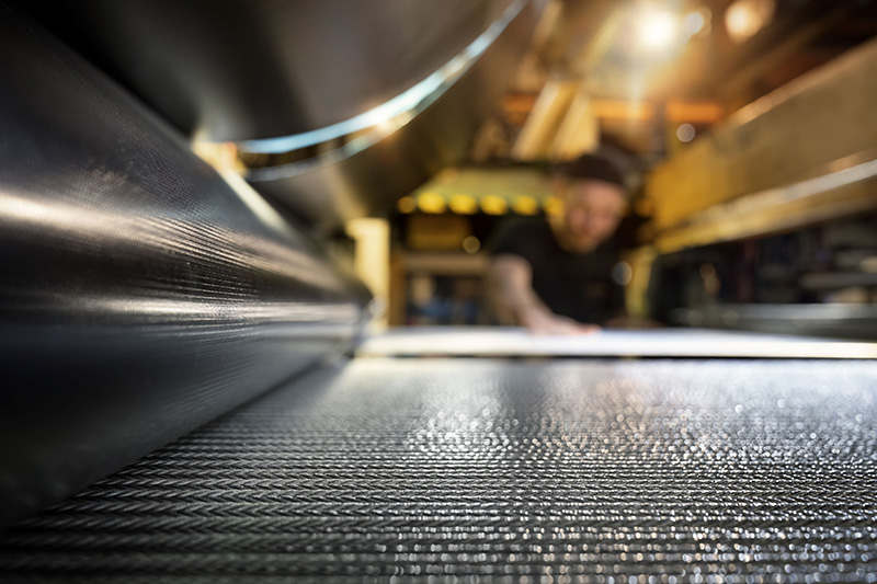 Ein Mitarbeiter überwacht in einer Industrieanlage die Produktion eines Bandes aus Gummimaterial.