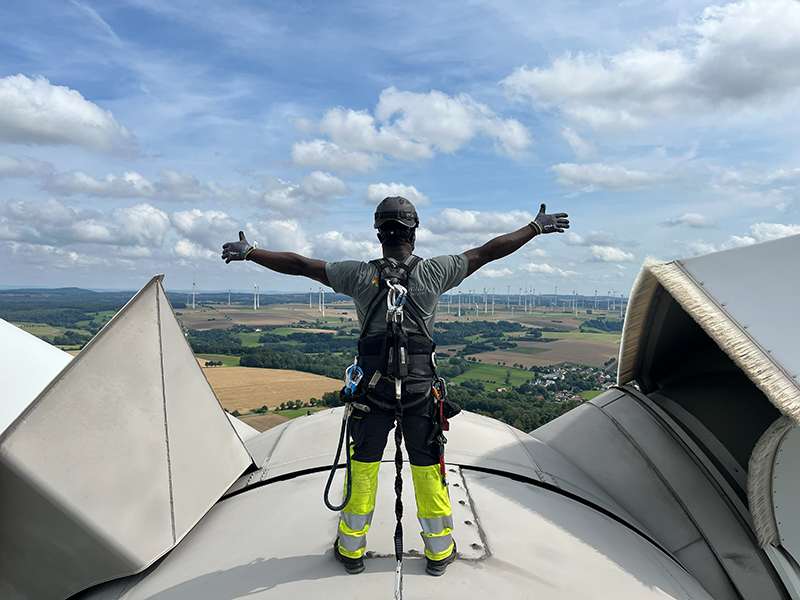 Ein Mann steht mit ausgestreckten Armen auf einer Windkraftanlage